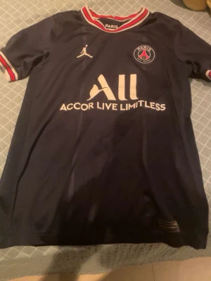 PSG x Jordan matchtröja marinblå  - Säljer en officiell Paris Saint-Germain x Jordan matchtröja i marinblått med röda och vita detaljer på krage och ärmslut. Tröjan har PSG-logga, Jordan-logga och sponsortryck framtill. Tillverkad i lätt polyester för maximal komfort. Äkta Storlek 137/147 eller barn M