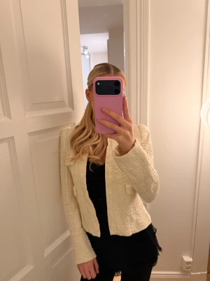 Krämvit kavaj från Zara - Säljer en krämvit kavaj med snygg tweedstruktur och croppad passform, från Zara. Jackan har två fickor framtill och är helfodrad. Perfekt att styla med svarta jeans eller kjol för en chic vibe. 