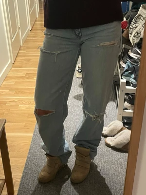 Ljusa ripped jeans från Zara - Säljer ett par ljusblå jeans från Zara med flera slitningar och hål på både fram- och baksida. Modellen är rak och lite loose fit med normal midja. Klassisk femficksdesign och tillverkade i bomull. Perfekta för en avslappnad och trendig look.
