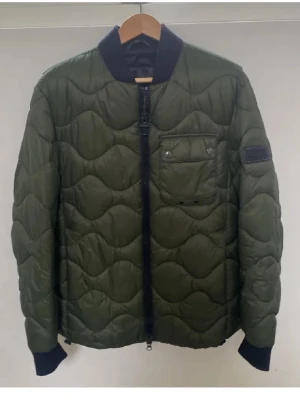 Grön quiltad bomberjacka Barbour  - Säljer en grön quiltad bomberjacka från Barbour International i storlek M. Jackan har svarta muddar, ribbad krage och dragkedja framtill. Den är helt oanvänd och priset kan självklart diskuteras! 