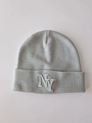 Grey Knit Beanie with NY Embroidery -  Grå stickad mössa med NY-brodyr  Stilren och bekväm grå stickad mössa med broderad NY-logga framtill. Klassisk modell med uppvikt kant som passar både dam och herr. Mjuk och stretchig – perfekt för höst och vinter. Lätt att matcha med de flesta outfits. 	•	Färg: Ljusgrå 	•	Passform: One size 	•	Skick: Mycket fint skick