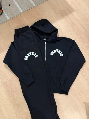 Svarta Corteiz mjukisbyxor S - Svarta mjukisbyxor från Corteiz med vit broderad logga på benet. Byxorna har resår i midjan och muddar vid bensluten för en skön och avslappnad passform. Tillverkade i mjukt bomullsmaterial som känns riktigt nice på. The set is a bit oversizef, and the pants are quite long! Keep in mind, it fits M or even L