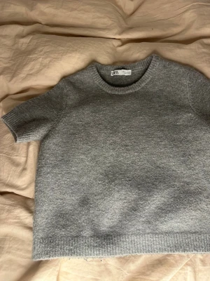 Grå stickad kortärmad tröja Zara - Säljer denna  gråa stickade tröjan från Zara med korta ärmar och rund hals. Tröjan är inprincip ny skick, den är lite nopprig på ryggen men inget större🥰🫰🏼 Obs! Tröjan är liten i storleken så den passar xxs och xs