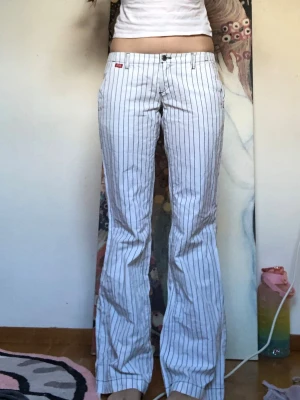 Randiga vita byxor från Miss Sixty - Säljer ett par vita byxor från Miss Sixty med tunna svarta vertikala ränder. Byxorna har låg midja och ett rakt snitt med lätt utsvängda ben. 