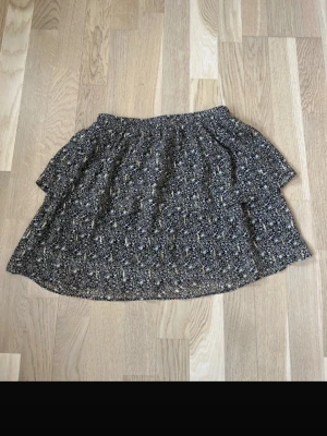 Mini volang kjol - Säljer denna volangkjol från SOFIE SCHNOOR. Svart med små blommor och guldiga blixtar. Använd en enstaka gång. Storlek 152 men passar XS-S. Nypris mellan 400-600