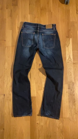 Nudie Jeans ”Slim Jim” - Säljer ett par mörkblå Nudie Jeans Slim Jim med klassisk Nudies klassiska design bakpå och en lätt snygg tvätt . Perfekta för dig som gillar stilrena jeans och en tidslös stil. Jeansen har inga hål eller fläckar och är som nya.  Storleken är W33 och L34. Skicka ifall du vill ha måtten eller vilka funderingar som helst!😊  !!Postas 24h inom köp!!