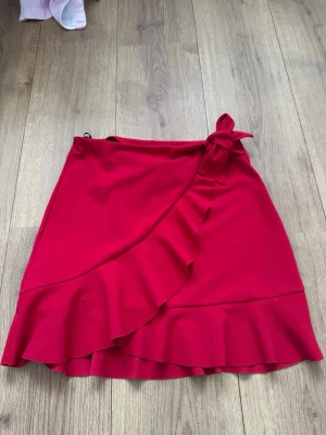 Röd omlottkjol med volang från Primark - Supersnygg röd kortkjol från Primark i omlottmodell med volangkant och knyt i sidan. ❤️pris kan diskuteras