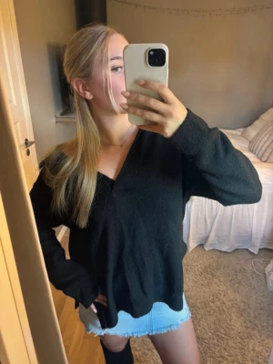 Svart stickad v-ringad tröja - En svart stickad tröja med v-ringning och krage. Tröjan har en loose passform och långa ärmar, perfekt att slänga på sig över ett linne eller t-shirt. Enkel och stilren design som funkar till många outfits.