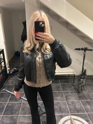 Svart croppad bomberjacka i skinn - Säljer en svart bomberjacka i skinn med ribbade muddar vid ärmslut och midja. Jackan har dragkedja framtill och en croppad passform som ger en cool och modern look. Perfekt till höst och vinter för dig som vill ha en stilren och edgy jacka. Väldigt svår att få tag på❤️storleken är L men sitter som en S