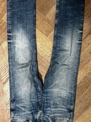 Blå skinny jeans med slitningar - Säljer ett par blå skinny jeans med snygga slitningar och tvättade detaljer längs benen. Jeansen har en klassisk femficksmodell och är tillverkade i stretchigt denimtyg för en tight passform. Perfekta till sneakers eller boots. 30 32  slim glenn