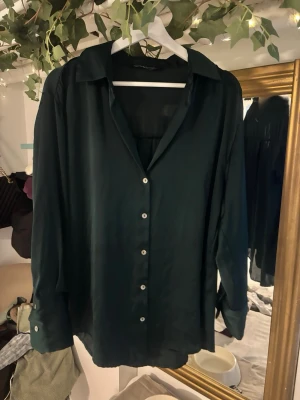 Mörkgrön skjorta från Zara i satin - Snygg mörkgrön skjorta från Zara i mjukt satinliknande material. Skjortan har klassisk krage, långa ärmar med breda manschetter och knappar framtill. Perfekt oversized fit för en chill och trendig look.