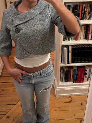 Grå croppad kavaj/bolero med stora knappar - Säljer en grå croppad kavaj/jacka/bolero som har trekvartsärm och en strukturerad krage som ger en unik look.