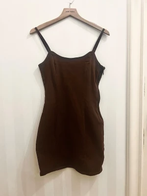 Brun klänning H&M Divided - Supersnygg brun kort klänning från H&M Divided. Figurnära modell med tunna axelband och enkel, stilren design. Perfekt att styla med en t-shirt under eller en stickad tröja över.