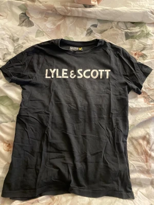 Svart Lyle & Scott t-shirt junior - Snygg svart t-shirt från Lyle & Scott med stor vit logga framtill. Klassisk rund hals och korta ärmar. Inga fläckar eller hål i tröjan, sälja pågrund utav att den aldrig kommer till användning. 