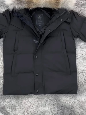 Svart dunjacka från Canada Goose - Säljer en svart dunjacka från Canada Goose med stor fluffig päls runt huvan. Jackan har långa ärmar, dragkedja och knappar framtill samt två stora fickor. Perfekt för kalla vinterdagar och riktigt snygg streetstil.