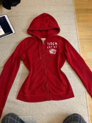 Snygg röd Abercrombie&Fitch zip up - Storlek L men passar som M. <3 Axelbredd: 39cm, Längd: 59cm. 