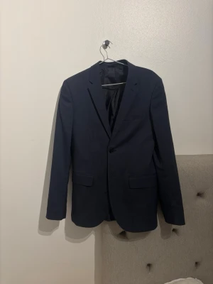 Mörkblå kavaj från H&M Skinny Fit - Snygg mörkblå kavaj från H&M i modellen Skinny Fit. Klassisk design med två fickor fram, en bröstficka och knäppning med en knapp. Perfekt för dig som gillar en smalare passform och stilren look.