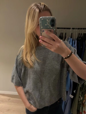 Grå stickad tröja från 157 - Mysig grå stickad tröja från 157 i storlek S. Tröjan har en loose passform med kortare, breda ärmar och rund halsringning. Perfekt att slänga på sig när det är lite kyligt ute.