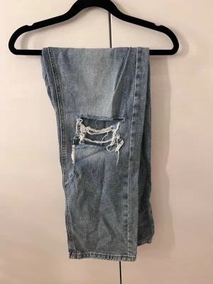 Ljusblå slitna jeans med hål - Säljer ett par ljusblå jeans med snygga slitningar och hål på låret och fickan. Jeansen har raka ben.