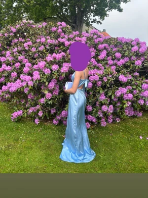 Ljusblå långklänning i satin - Säljer en elegant ljusblå långklänning i satin med smala axelband och v-ringning. Klänningen har öppen rygg och en knytning i ryggen som är en sån fin detaljj. Perfekt för bal eller student! Superfin passform och skimrande material. Hör av er för mer bilder eller frågor!