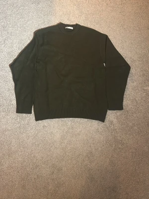 Mörkgrön stickad tröja från Zara - En enkel och stilren mörkgrön stickad tröja från Zara. Tröjan har rund halsringning, ribbade muddar vid ärmslut och nederkant samt lång ärm. Perfekt för lager på lager under höst och vinter.