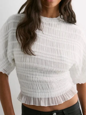 Vit plisserad blus med volangkant - Säljer en superfin vit blus med plisserad struktur och volangkant nedtill. Från Nelly i storlek xs