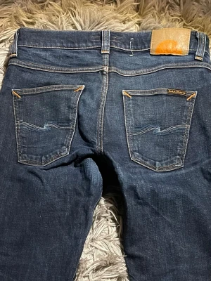 Nudie Jeans Slim 31/32 - Säljer ett par mörkblå ”Lean Dean” från Nudie Jeans i modellen slim fit. Dry denim vilket är typ som Raw denim, omsydda i benen och lagade på baksidan. Jeansen är slim i passformen.