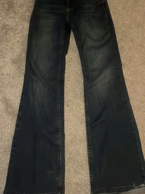 Blå bootcut jeans med rå kant - Säljer ett par mörkblå jeans med bootcut passform och rå, fransig kant i midjan. Jeansen har klassiska fem fickor, kontrastsömmar och är tillverkade i ett slitstarkt demintyg 