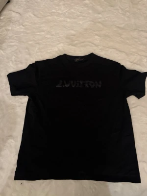 Lv T-shirt - Skick: mycket bra, inga fläckar / hål Detaljer: 	•	Färg: Svart (texten är svart också men blir blå i solljus) 	•	Material: bomull 	•	Passform: regular fit 	•	storlek: M (Passar medium)  Plagget kommer från rök- och djurfritt hem.  📦 Frakt: skickas samma dag om köp går igenom innan 18.00 💬 Frågor: Hör av dig om du vill ha fler bilder eller mått 🤝 Paketpris: Samfraktar gärna vid flera köp 