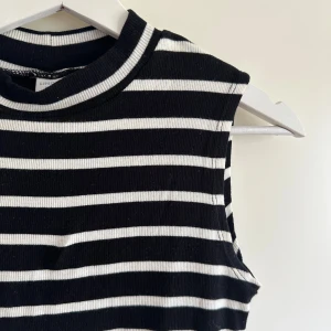 Randig ärmlös klänning från Lindex - Svartvit klänning från Lindex med horisontella ränder och ribbad struktur. Modellen är rak och slutar ovanför knäna, med en högre rund halsringning. Perfekt för dig som gillar enkel men snygg stil. Size 152