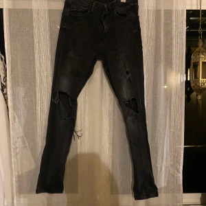 Svarta skinny jeans från FSBN 32/30 - Svarta skinny jeans från FSBN med slitna detaljer och stora hål på båda knäna. Jeansen har klassisk femficksdesign, dragkedja och knapp med FSBN-logga. Snyggt tvättade för en cool, lite ruff look. Perfekta för dig som gillar streetstyle.