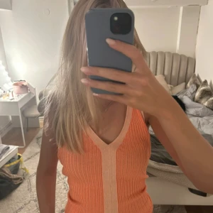 Ribbad orange ärmlös linnetopp - Säljer en snygg ribbad linnetopp i orange med ljusare aprikosfärgad kant och mittsöm. Toppen har v-ringning och är ärmlös, perfekt för varma dagar. Materialet är stretchigt och sitter skönt mot kroppen. Superfin att styla med jeans eller kjol!