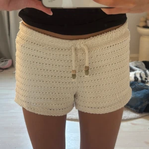 Vita virkade shorts med snörning - Säljer ett par vita virkade shorts med snygg snörning i midjan och trädetaljer på snörena. De är midwaist och har en loose passform, perfekta för sommaren. Materialet är mjukt och luftigt, vilket gör dem riktigt sköna och lätta att bära. Stlk 152 cm