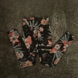 Stronger  - Snygga leggings med svart bas och färgglatt blommönster i orange, vitt och grönt. Hög midja och stretchigt material som sitter tajt och bekvämt. Perfekta för att sticka ut med en cool och trendig look. Väl använd 