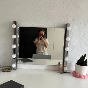 Sminkspegel med LED-belysning - Elegant sminkspegel med inbyggd LED-belysning längs sidorna för optimal makeupbelysning. Spegeln är i mycket gott skick utan synliga repor eller skador. Perfekt för sminkbordet och ger ett professionellt ljus. Fästen för väggmontering medföljer. Från Ikea 