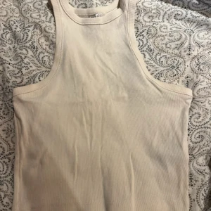 Beige ribbad linnetopp från Divided - Säljer en beige ribbad linnetopp från Divided, H&M. Toppen är ärmlös med rund halsringning och croppad passform. Perfekt att styla med jeans eller kjol för en enkel och clean look.