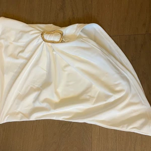 Vit tubetop med gulddetalj från Amisu - Supersnygg vit tubetop från Amisu med en unik guldfärgad metallring framtill som cool detalj. Den är helt ny. Inte använt en ända gång men min kompis klippte av lappen utan att jag visste. Den e i storlek s. 