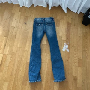 Lågmidjade bootcut jeans med fickdetaljer - Snygga blå bootcut jeans med trendig  ficksdesign och coola ficklock bak. Jeansen har en lätt tvättad look och är tillverkade i mjukt denimtyg. Perfekta för dig som gillar en avslappnad men trendig stil. Dom är köpta på barnavdelningen i 170  men skulle säga att de passar xs-s 