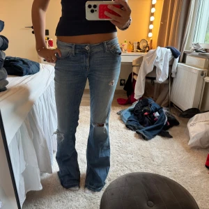 Blå bootcut jeans med slitningar - Snygga blå bootcut jeans med slitningar på båda knäna och fransig nederkant. Lågmidjade och i klassisk jeansmodell med fem fickor. Perfekta för en avslappnad och trendig look.