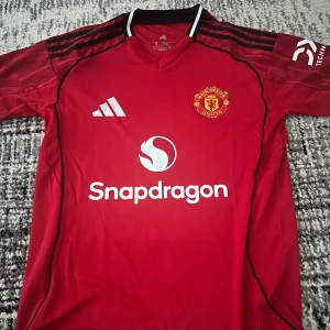 Manchester United Adidas matchtröja 25/26 - Här så säljer jag en ny manchester united 25/26 hemmatröja, säljer eftersom den passar inte mig, använt bara 1 gång. Behöver pengarna snabbt så skriv vid vilken pris ni vill köpa den, pris kan såklart diskuteras och om du bor nära haningen så kan vi mötas upp ananrs köp via appen.