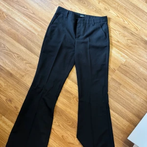 Svarta bootcut kostymbyxor Gina Tricot - Svarta kostymbyxor från Gina Tricot i storlek 38. Byxorna har bootcut-modell med normal passform, hällor för bälte och klassiska fickor fram. Perfekta för en clean och stilren look.