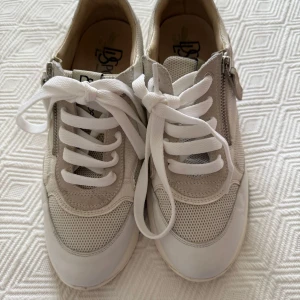 Vita och beige sneakers från DLSport - Snygga sneakers från DLSport i vitt och beige med detaljer i skinn, mocka och mesh. Skorna har vita snören, dragkedja på sidan och en chunky sula i vitt och grått. Perfekta för dig som gillar en sportig och stilren look.