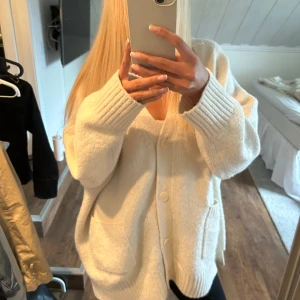 Beige stickad kofta med knappar - Mysig vit stickad kofta med stora knappar framtill och två fickor. Koftan har en loose passform och breda ribbade muddar vid ärmslut och nederkant. Perfekt för lager-på-lager och chill dagar. Jag är normalt en S/M så denna storlek är en perfekt storlek för en snygg oversize passform! 💕