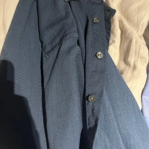 Blå skjorta från Bruun & Stengade - Snygg blå skjorta från Bruun & Stengade i klassisk modell. Skjortan har knappar framtill och är tillverkad i ett strukturerat bomullstyg. Perfekt för dig som gillar stilrena och enkla plagg med en modern touch. Använd två gånger.