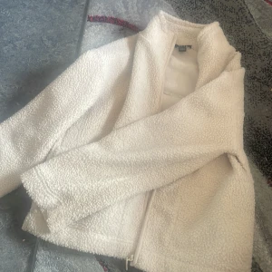 Vit teddyjacka från Amisu XS - Mysig vit teddyjacka från Amisu i storlek XS. Jackan har dragkedja framtill, hög krage och är tillverkad i fluffigt teddy-material som ger en riktigt skön vibe. Perfekt för kyliga dagar när du vill vara både varm och snygg.