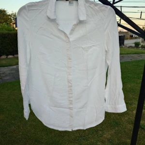 Vit skjorta från H&M DIVIDED - Klassisk vit skjorta från H&M DIVIDED i storlek 36. Skjortan har lång ärm, bröstficka och knappar hela vägen framtill. Tillverkad i mjuk bomull med avslappnad passform och krage. Perfekt för en clean och enkel look.