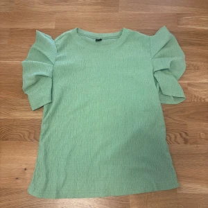 Grön ribbad topp med volymärmar Shein - Snygg ljusgrön topp från Shein i storlek S. Toppen har ribbad struktur och korta volymärmar som ger en cool och trendig look. Perfekt att styla med jeans eller kjol för en fräsch vibe. Materialet är mjukt och stretchigt för extra komfort.