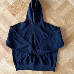 Svart hoodie med huva från Bershka - En klassisk svart hoodie med huva och långa ärmar. Tröjan har ribbade muddar vid ärmslut och nederkant, vilket ger en skön och avslappnad passform. Perfekt för dig som gillar en enkel och stilren look.
