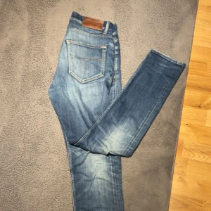 Blå jeans med slitningar - Snygga blå jeans med ljusa partier, klassisk femficksmodell och läderpatch i midjan. Jeansen har en rak passform och är tillverkade i robust denim. Perfekta för en avslappnad stil. Jeansen har även ett litet hål som knappt syns. Byxorna är i använt skick men sitter extremt bra för dig som är runt 180cm. Skulle säga att skicket är 6,7/10.