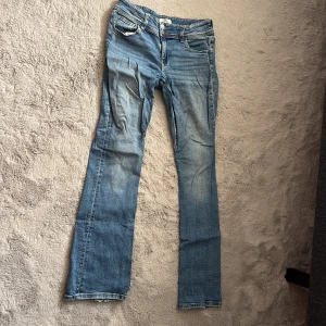 Blå bootcut jeans från Gina Tricot - Snygga blå jeans från Gina Tricot i bootcut-modell med klassisk femficksdesign och dubbla knappar fram. Jeansen har ljusa slitningar och bakfickor med lock och knapp. Perfekta för dig som gillar en avslappnad men trendig look.